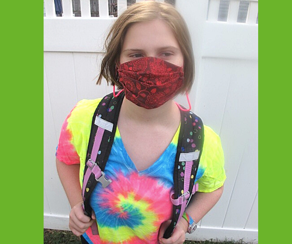 Girl wearing a tie dye shirt and back pack wearing a mask with the lanyard